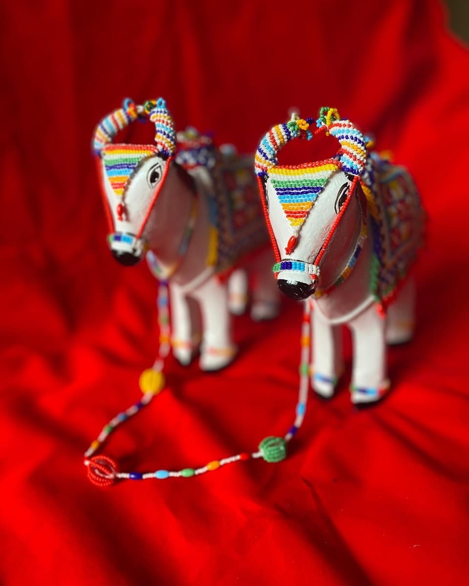 Two white bull figurines decorated with colourful beads on their horns, faces, and bodies connected by beaded harness