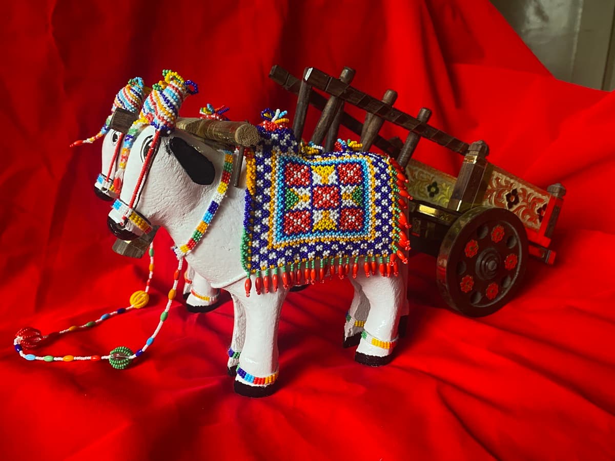 Wooden bullock cart with bull decorated in colourful beadwork harnesses on a red fabric background