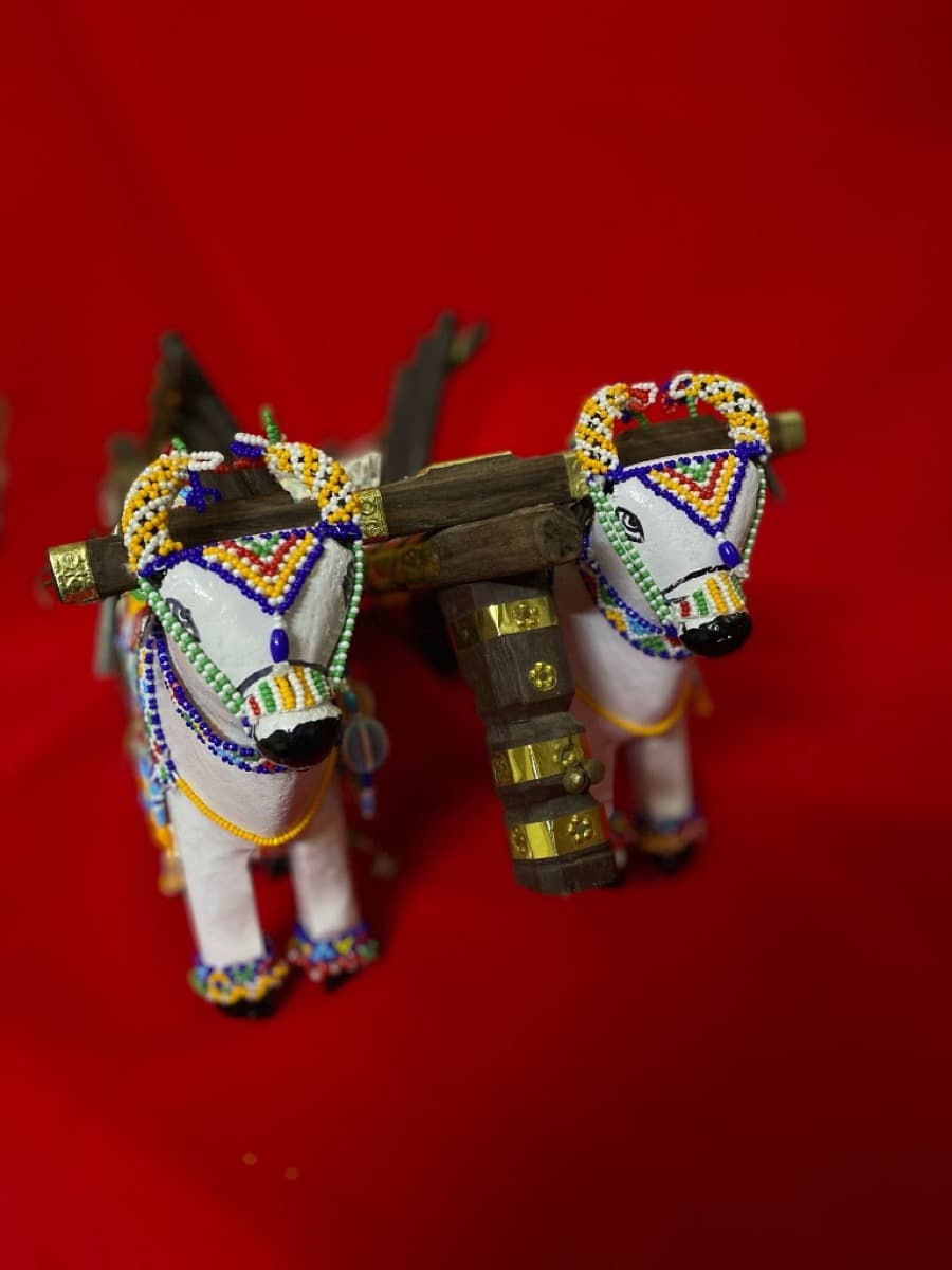 Pair of white beaded bulls connected by a wooden yoke and cart, decorated with colourful beaded harnesses and ornaments