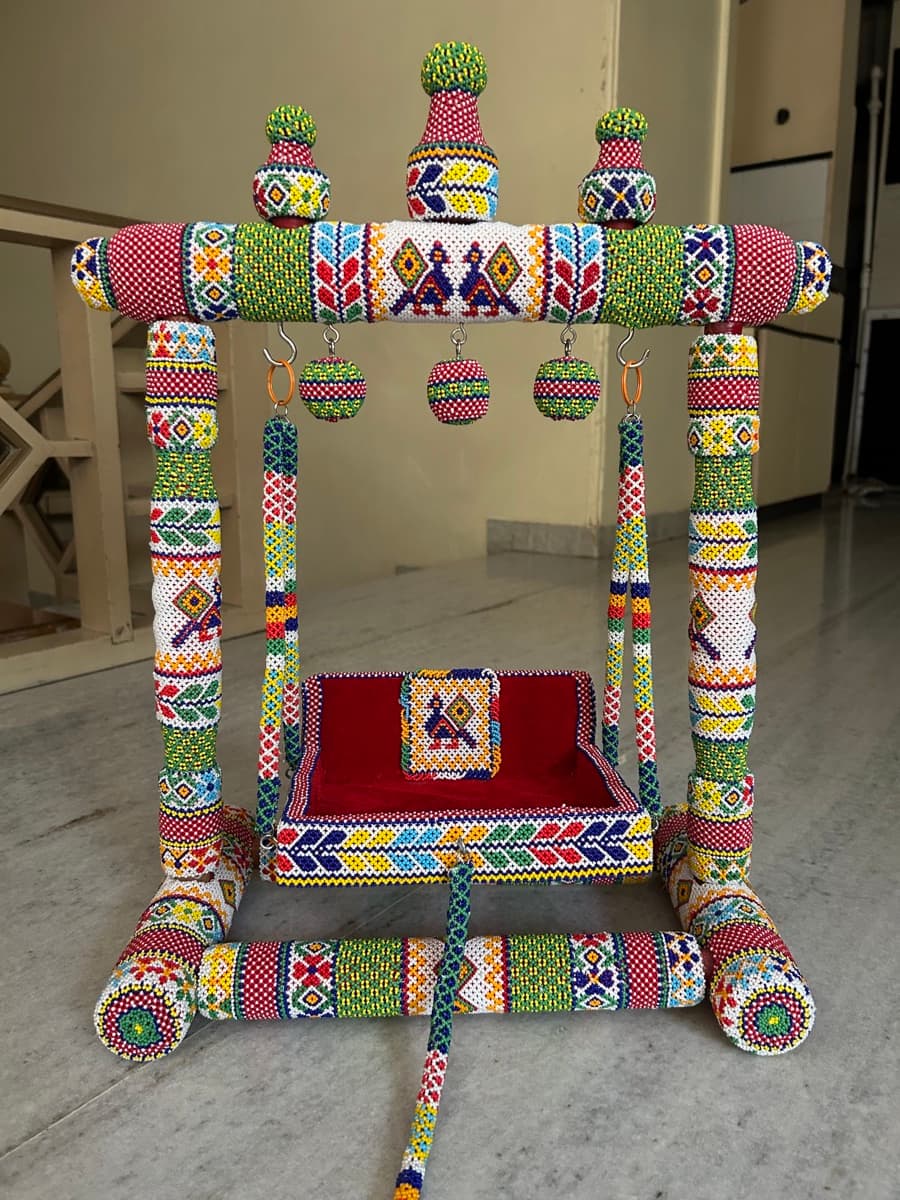 Traditional Gujarati jhula decorated with detailed multicoloured beadwork in floral and geometric designs with a red velvet seat