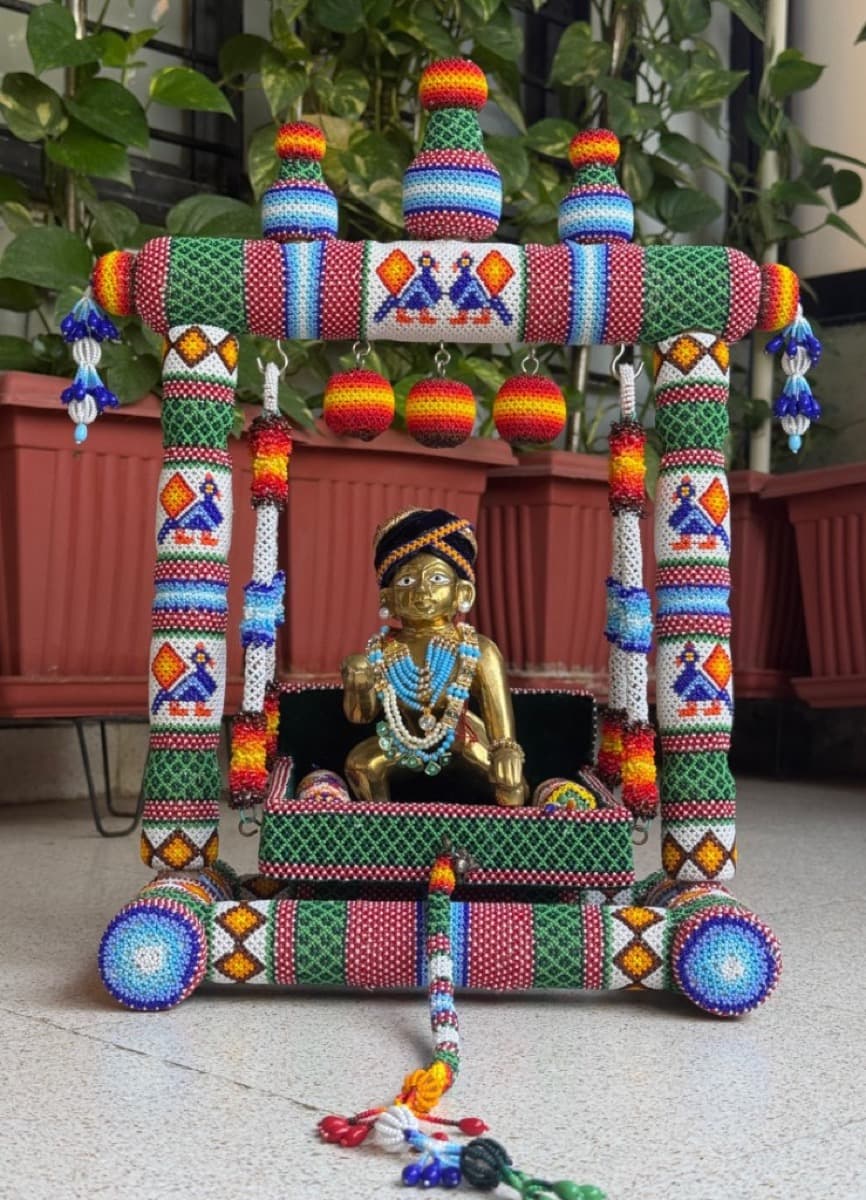 Beaded cradle-swing for Laddu Gopal featuring colourful moti kaam pillars, rainbow spheres, and a seated brass Krishna idol