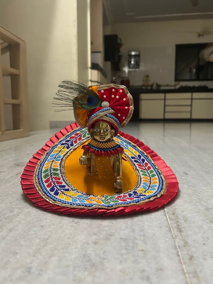 Laddu Gopal brass murti dressed in a golden beaded vagha with red satin border and peacock feather crown