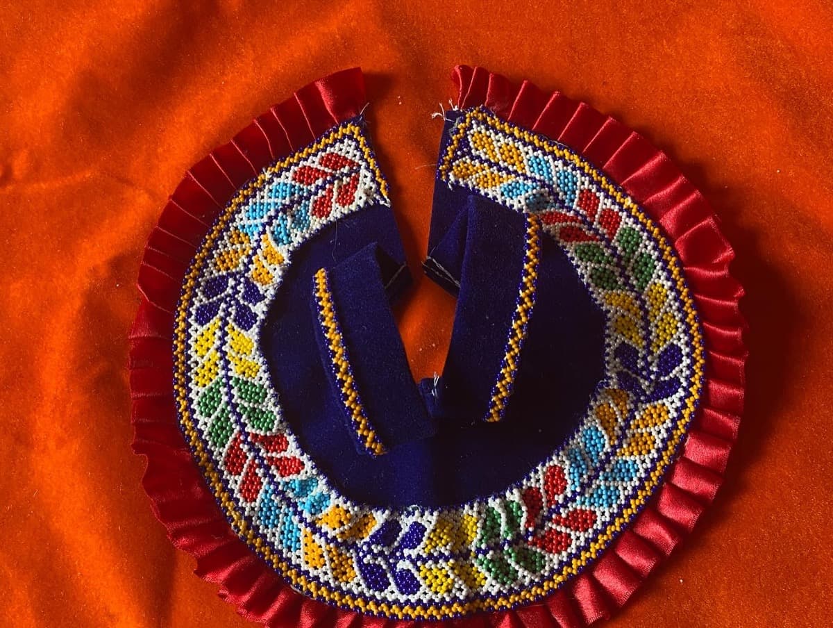 Circular Laddu Gopal singhasan with multicoloured beadwork forming leaf patterns on dark blue fabric with red satin ruffle
