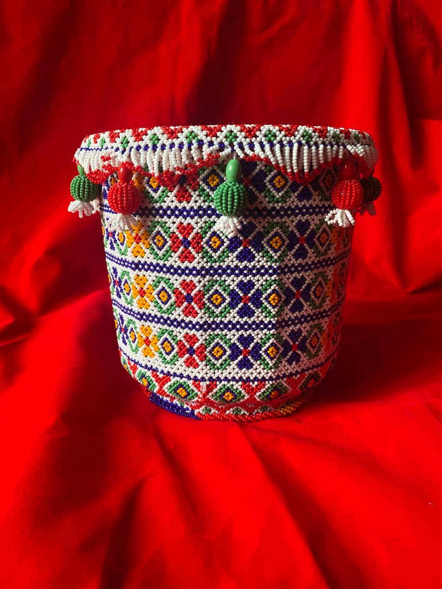 Beaded matka cover with geometric patterns and hanging bead tassels on red fabric