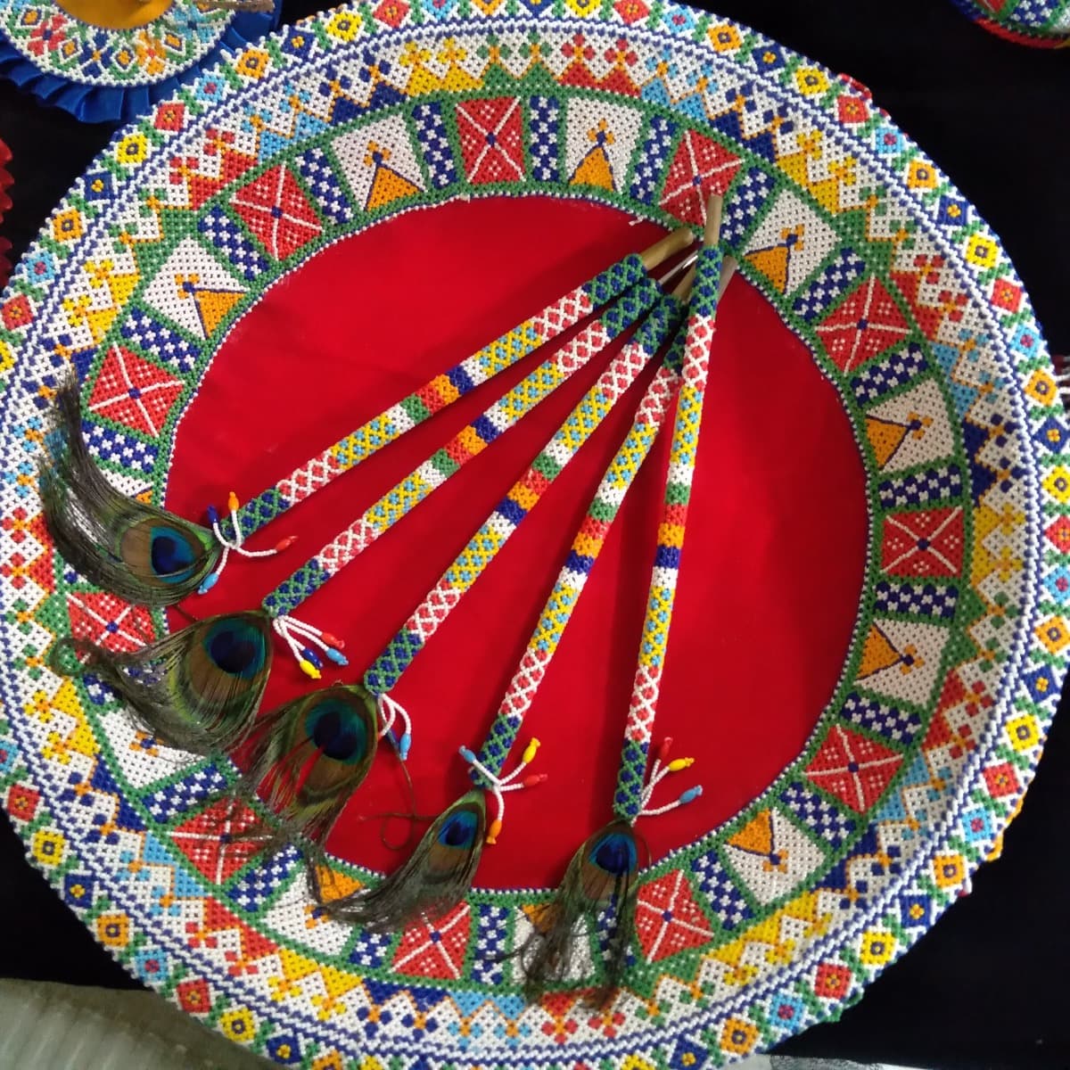 Set of five colourful beaded sticks with peacock feathers arranged on a round beaded mat