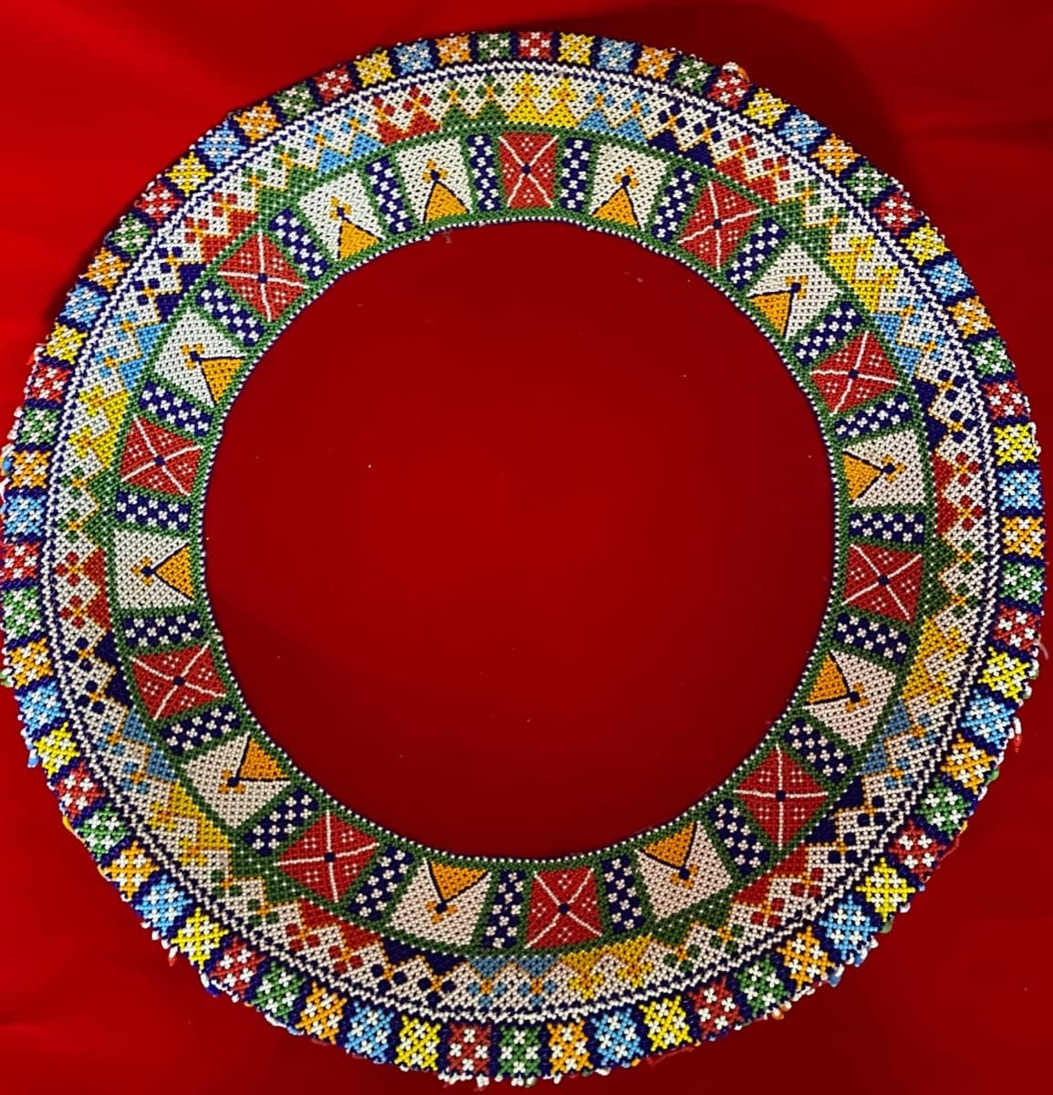 Circular moti bharat tras with concentric geometric beadwork rings in vibrant colours on a red background