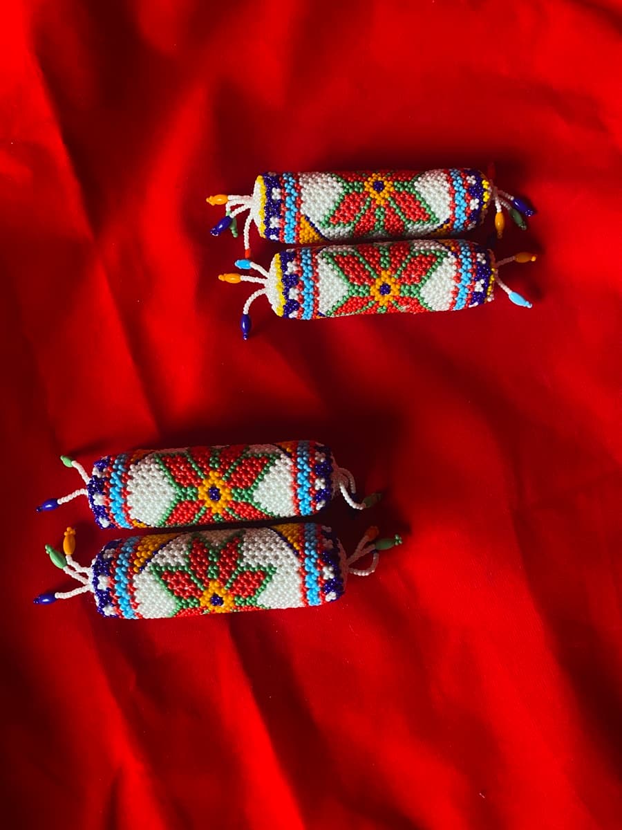 Four cylindrical beadwork pieces with colourful floral patterns on a bright red fabric