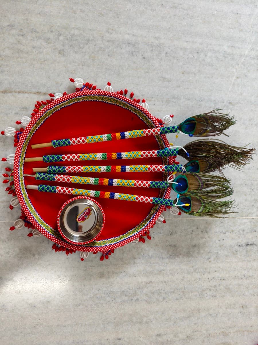 Moti bharat pithi saliya set — beaded bamboo sticks with peacock feathers on a decorated tras